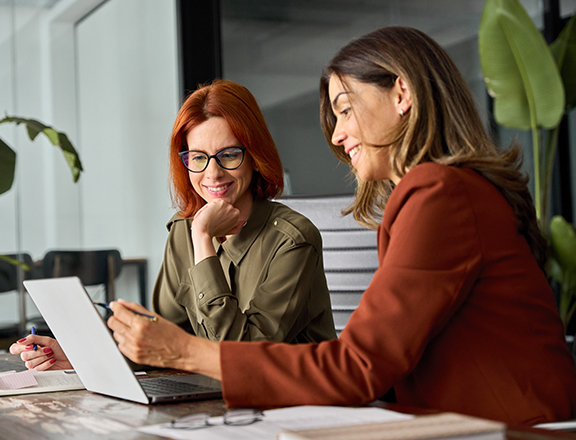 Two happy busy female employees working together using computer planning project.
